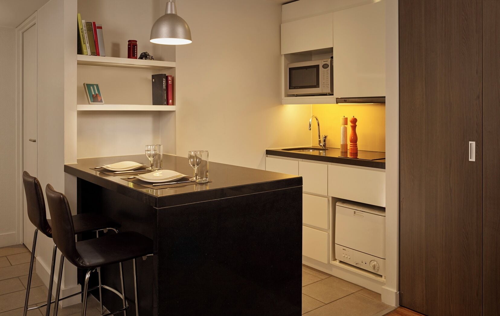 A compact kitchen with a central island, a microwave, a sink, and a bookshelf.