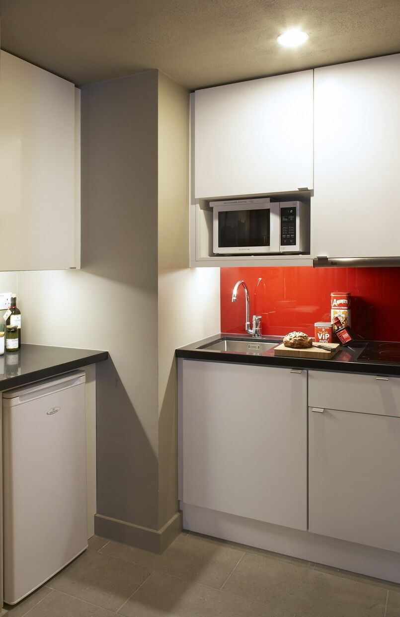 Een compacte keuken met witte kastjes, een magnetron, een spoelbak en een kleine vaatwasser.