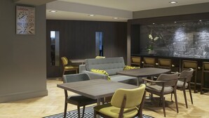 A modern dining area with a central table, chairs, and a sofa. There is a large clock on the wall and a cityscape artwork on the wall. - Citadines Trafalgar Square London (London)