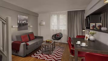 A modern living room with a grey sofa, red cushions, a dining table with red chairs, a coffee table, and a red and white chevron rug.