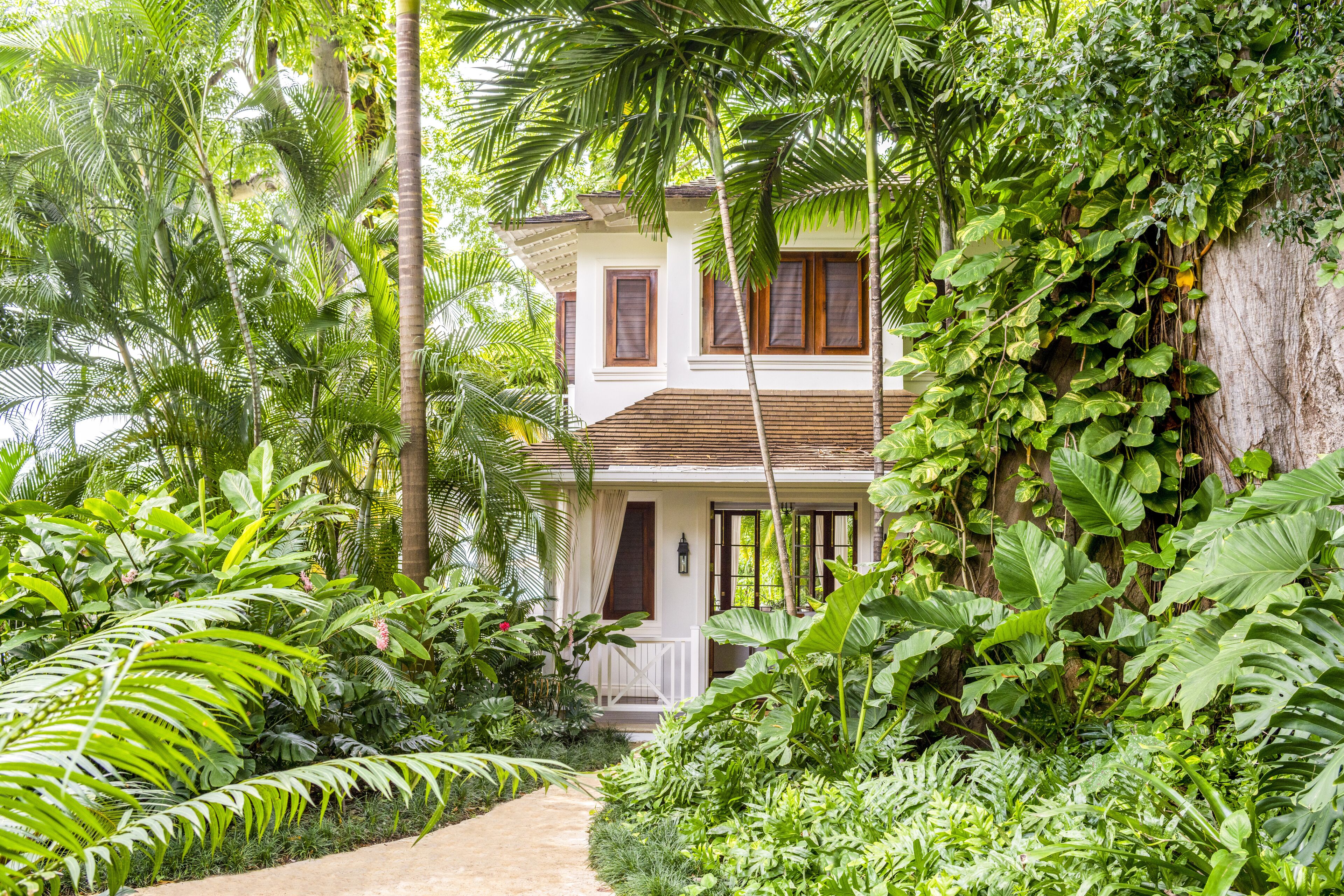 A two-story house surrounded by lush tropical vegetation.