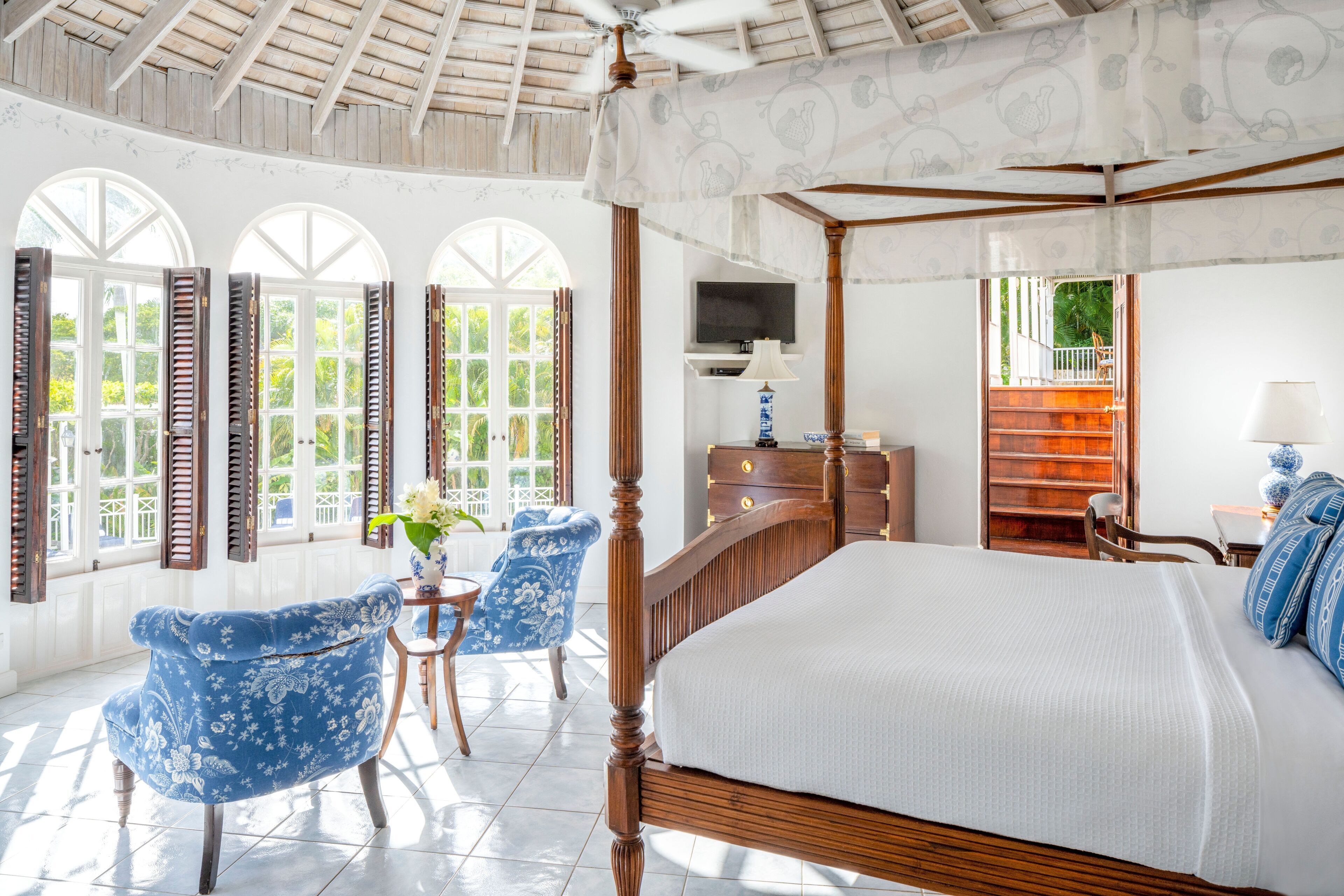A spacious bedroom with a four-poster bed, a television, and a small table with a chair.