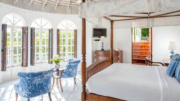 A spacious bedroom with a four-poster bed, a television, and a small table with a chair.