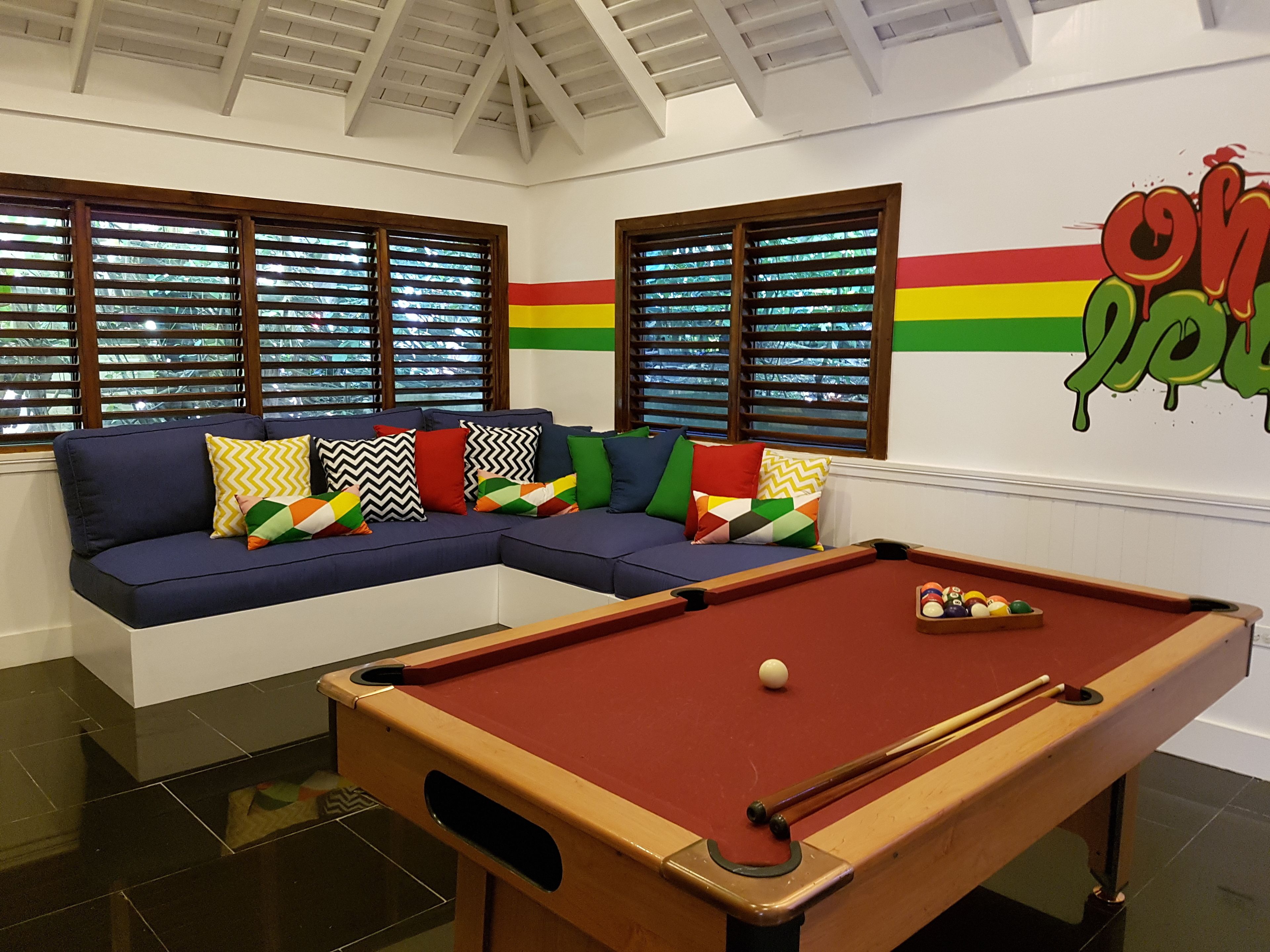 A pool table in a room with a sectional sofa and windows with blinds.