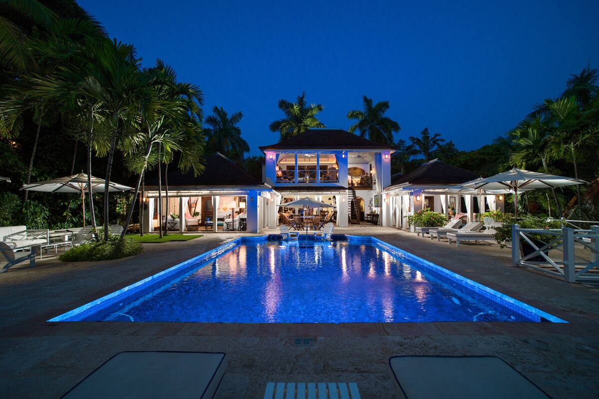 Un espace aménagé au bord de la piscine, comprenant une piscine, des chaises longues, des parasols et un bâtiment à plusieurs niveaux doté d’un espace de détente extérieur.