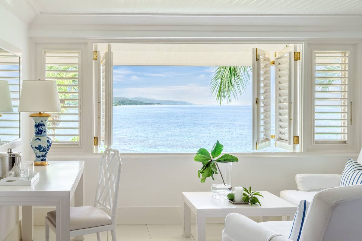 Une pièce avec vue sur la mer, des meubles blancs et un vase bleu et blanc posé sur une table.