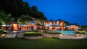 A large, multi-story house with a swimming pool, outdoor seating, and a well-lit entrance. - Round Hill Hotel And Villas (Montego Bay)