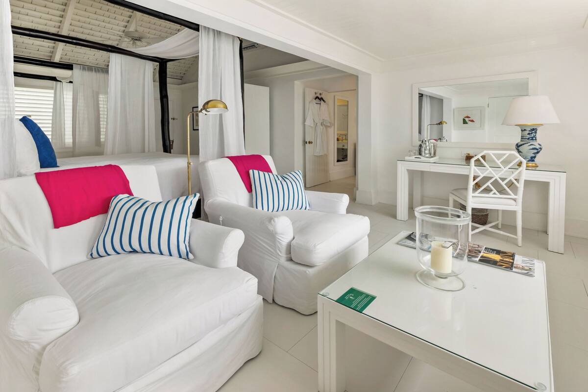 Une pièce moderne et bien éclairée, avec un ensemble de canapés blancs, une table basse en verre et un bureau blanc doté d’une lampe.