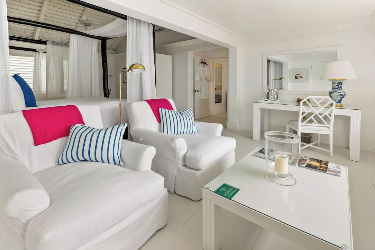 A modern, well-lit room with a white sofa set, a glass coffee table, and a white desk with a lamp.