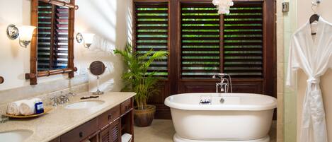 A bathroom with a freestanding bathtub, a large mirror, a potted plant, and a robe hanging on the wall.