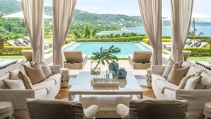 A luxurious outdoor seating area with a pool, white furniture, and a scenic view of the ocean and hills. - Round Hill Hotel And Villas (Montego Bay)