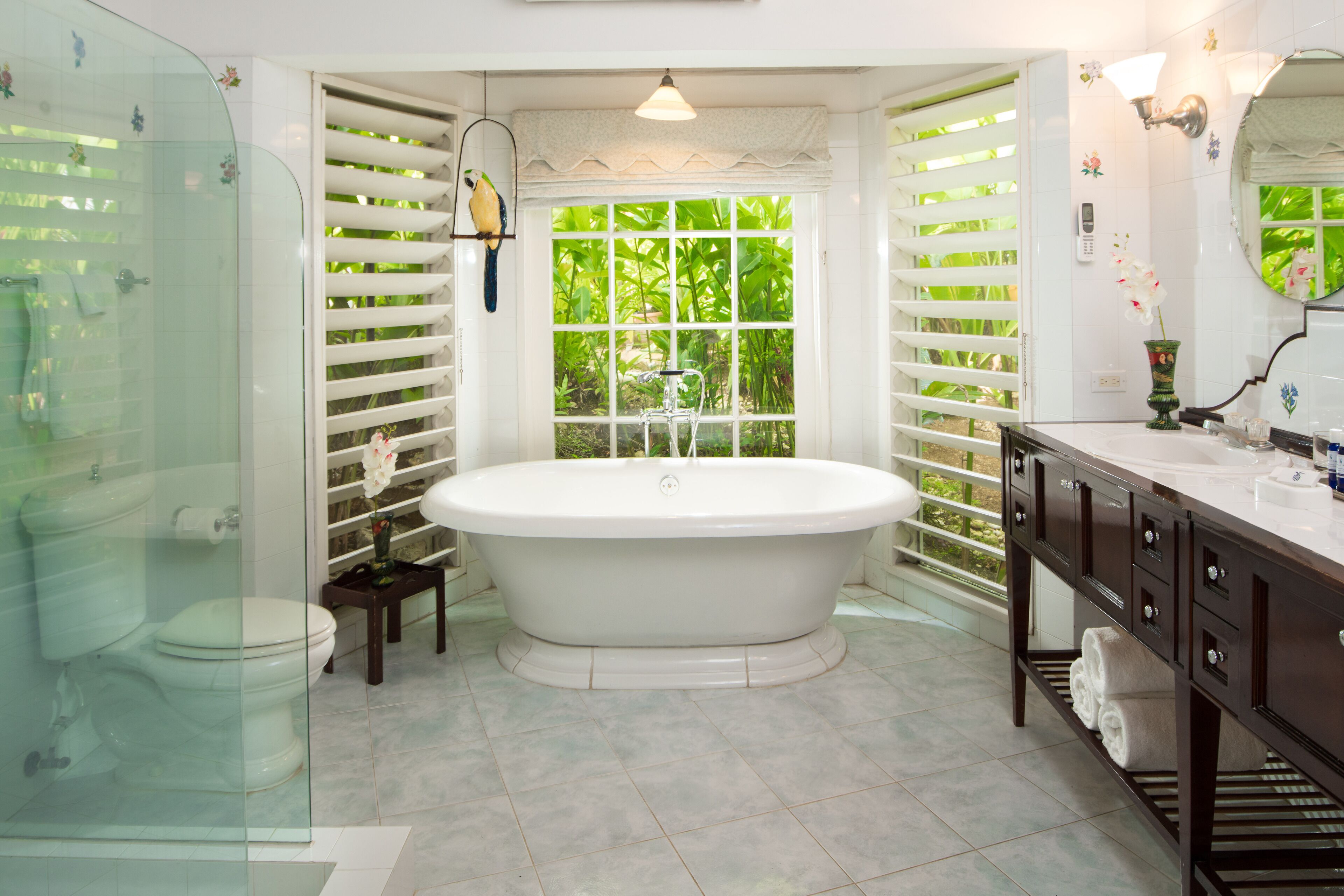 A bathroom with a freestanding bathtub, a glass shower enclosure, a vanity with a mirror, and a window with a view of greenery.