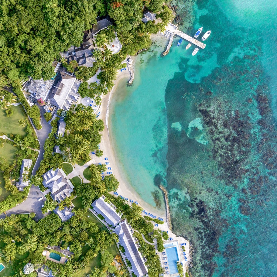 An aerial view of a resort with multiple buildings, a beach, and clear turquoise waters.