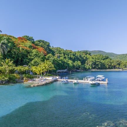 A coastal area with boats docked at a pier, surrounded by lush greenery and a clear blue sky.