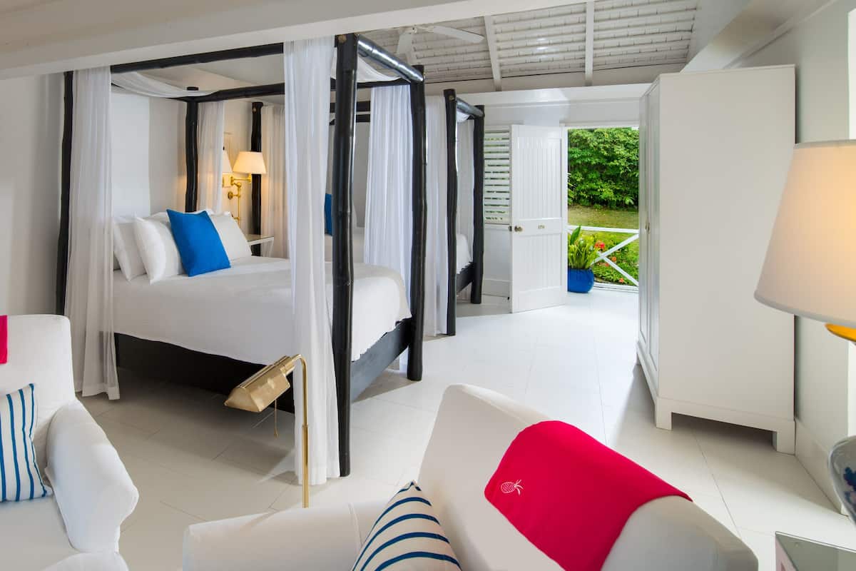 Une chambre à coucher avec un lit, un coin salon avec des fauteuils, une table de chevet et une vue sur l’extérieur.