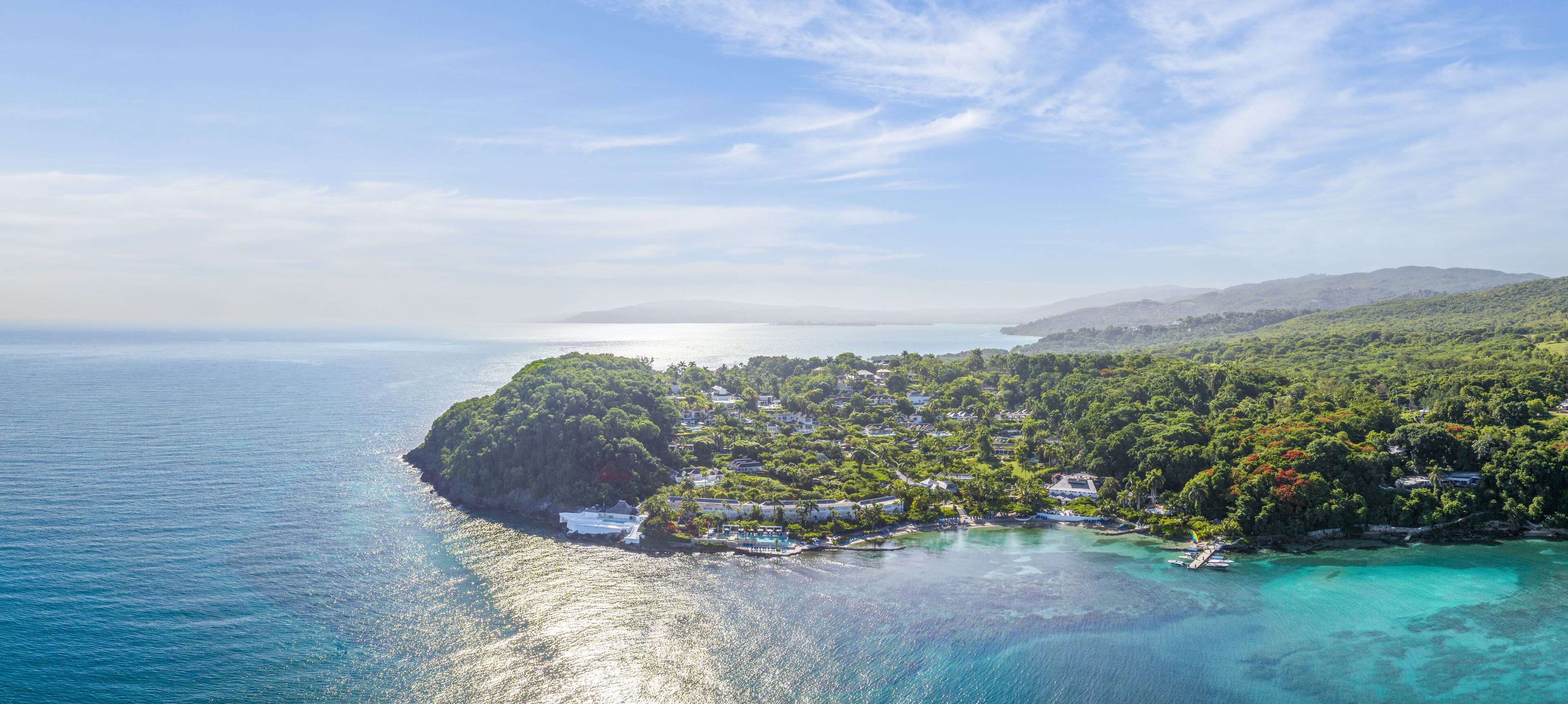 A coastal town with houses along the shoreline, a small island, and clear turquoise waters.
