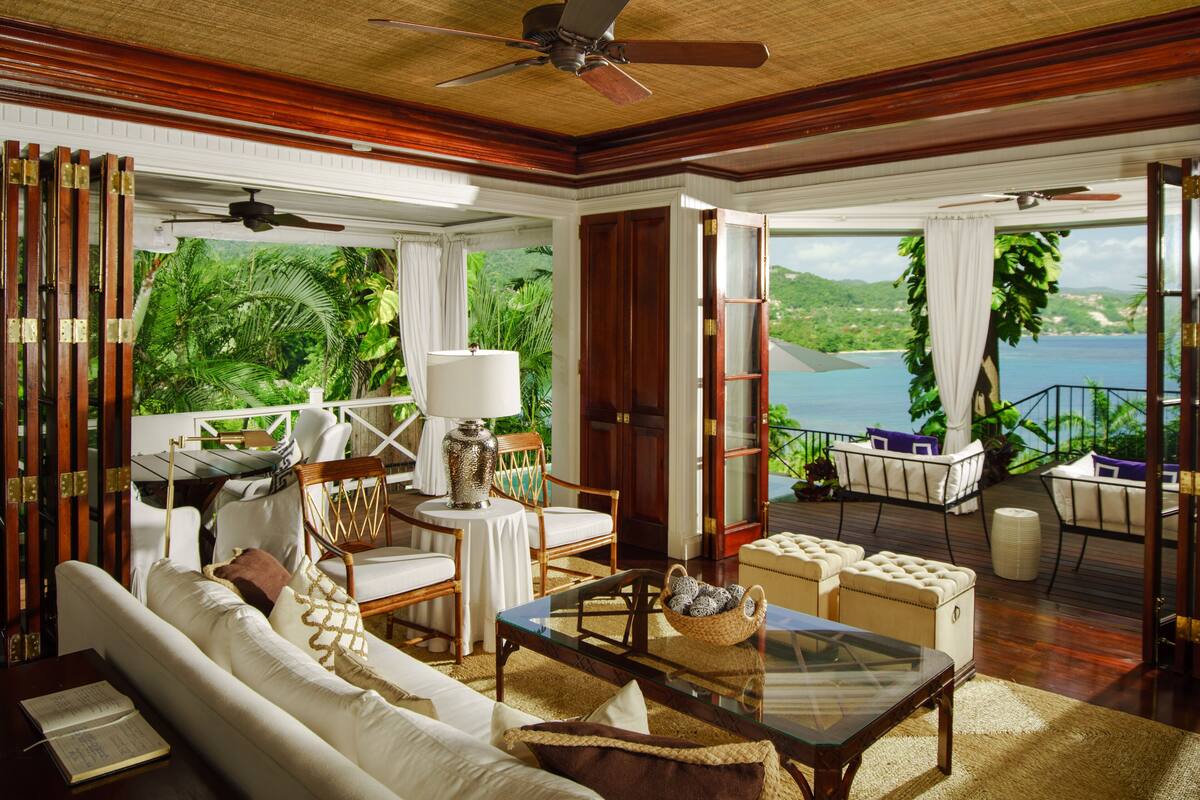Un salon spacieux, doté d’un grand canapé, d’une table basse et offrant une vue sur un paysage tropical grâce à une porte vitrée.