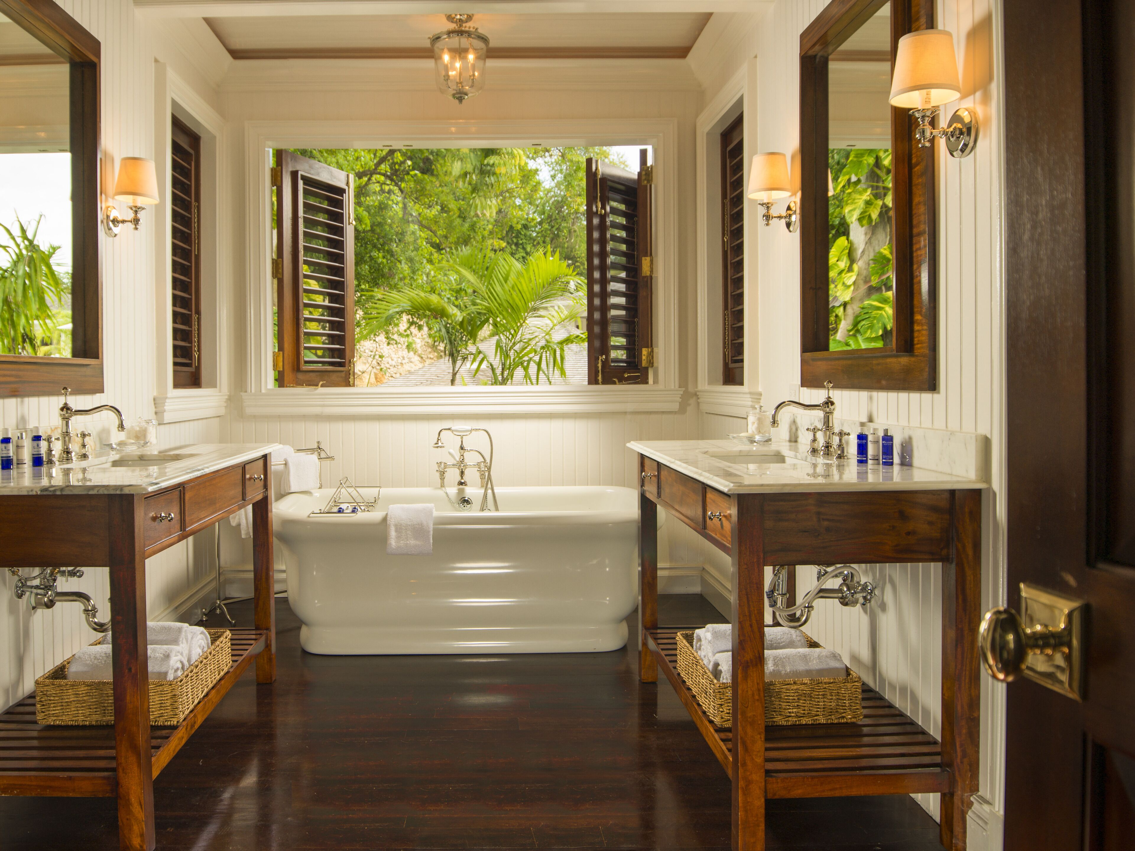 A bathroom with a large bathtub, two sinks, and a window with shutters.