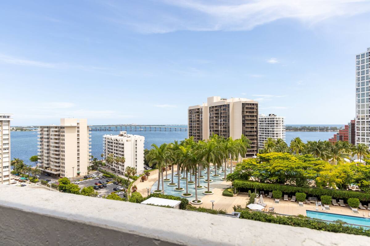 A high-rise hotel with a pool area, palm trees, and a view of the water and a bridge.