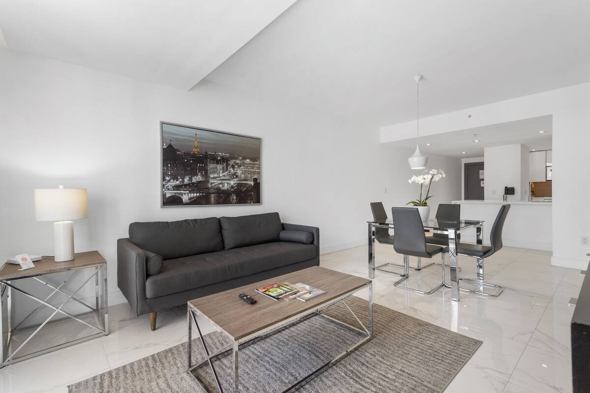 A modern living room with a gray sofa, a coffee table, and a dining area with a glass table and chairs.