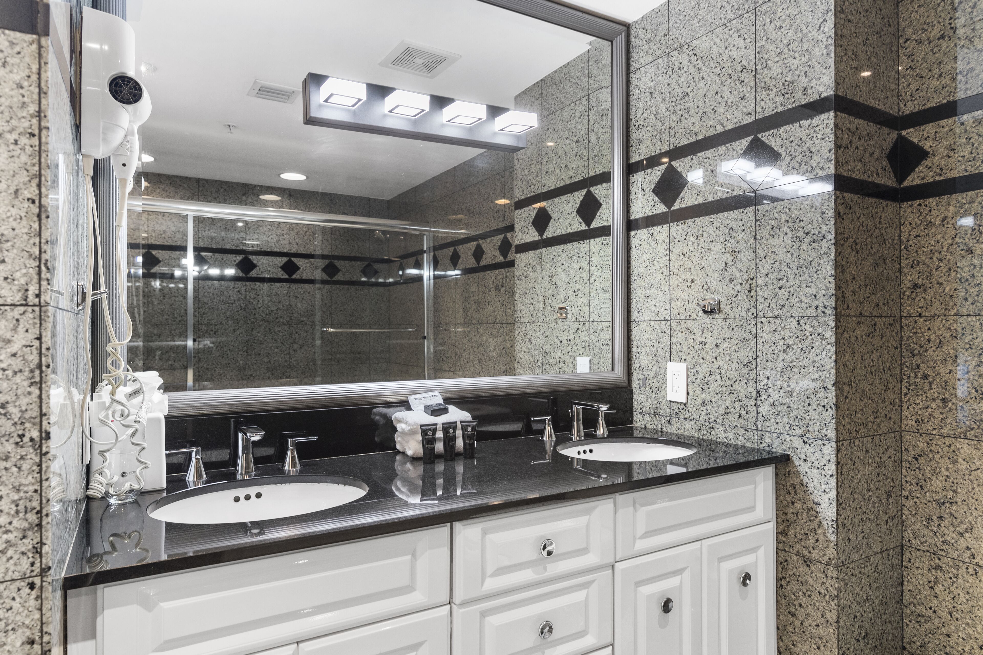 Une salle de bain moderne avec deux lavabos, un grand miroir et un sèche-cheveux.