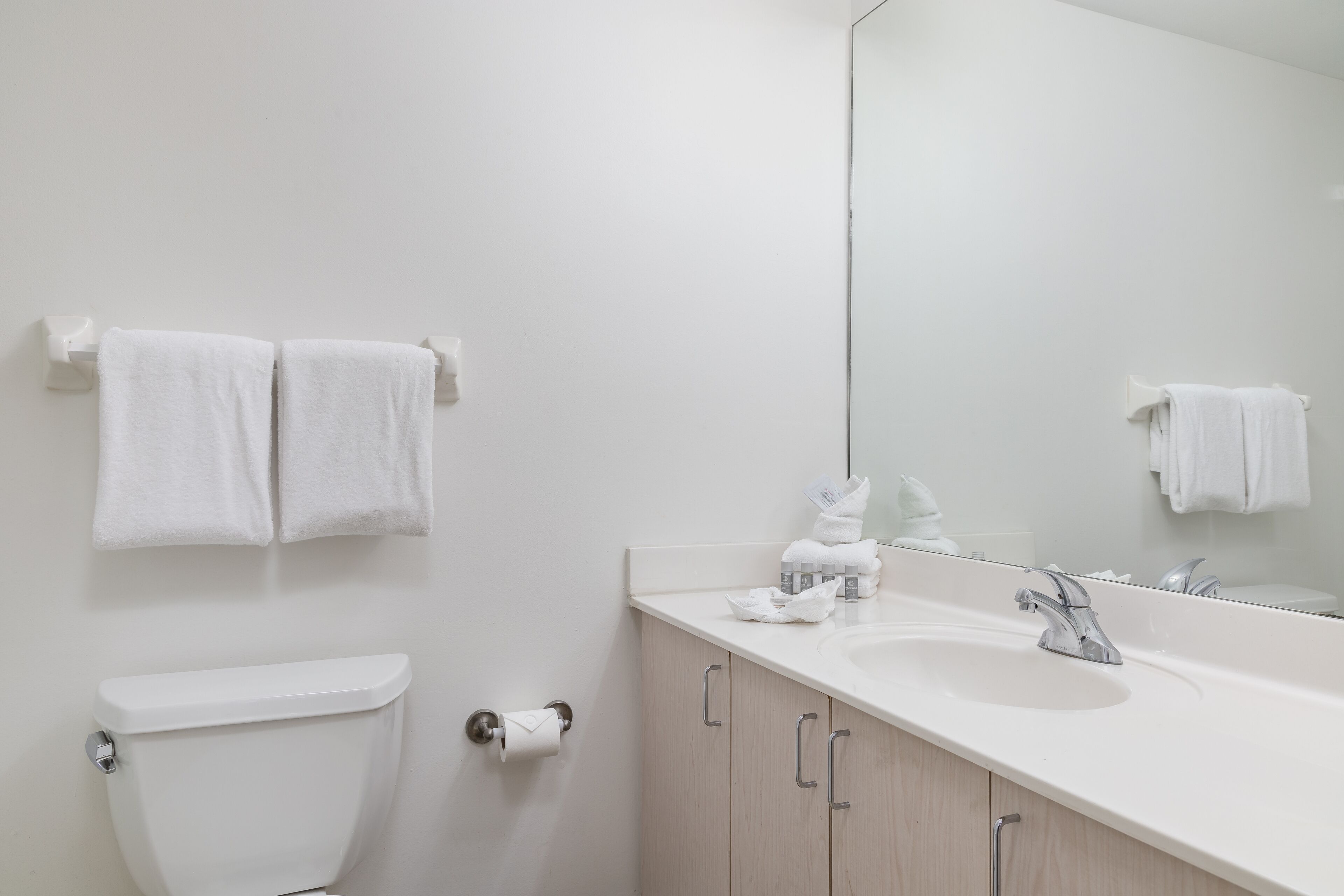 A modern bathroom with a toilet, sink, and mirror. There are two towels hanging on the wall.