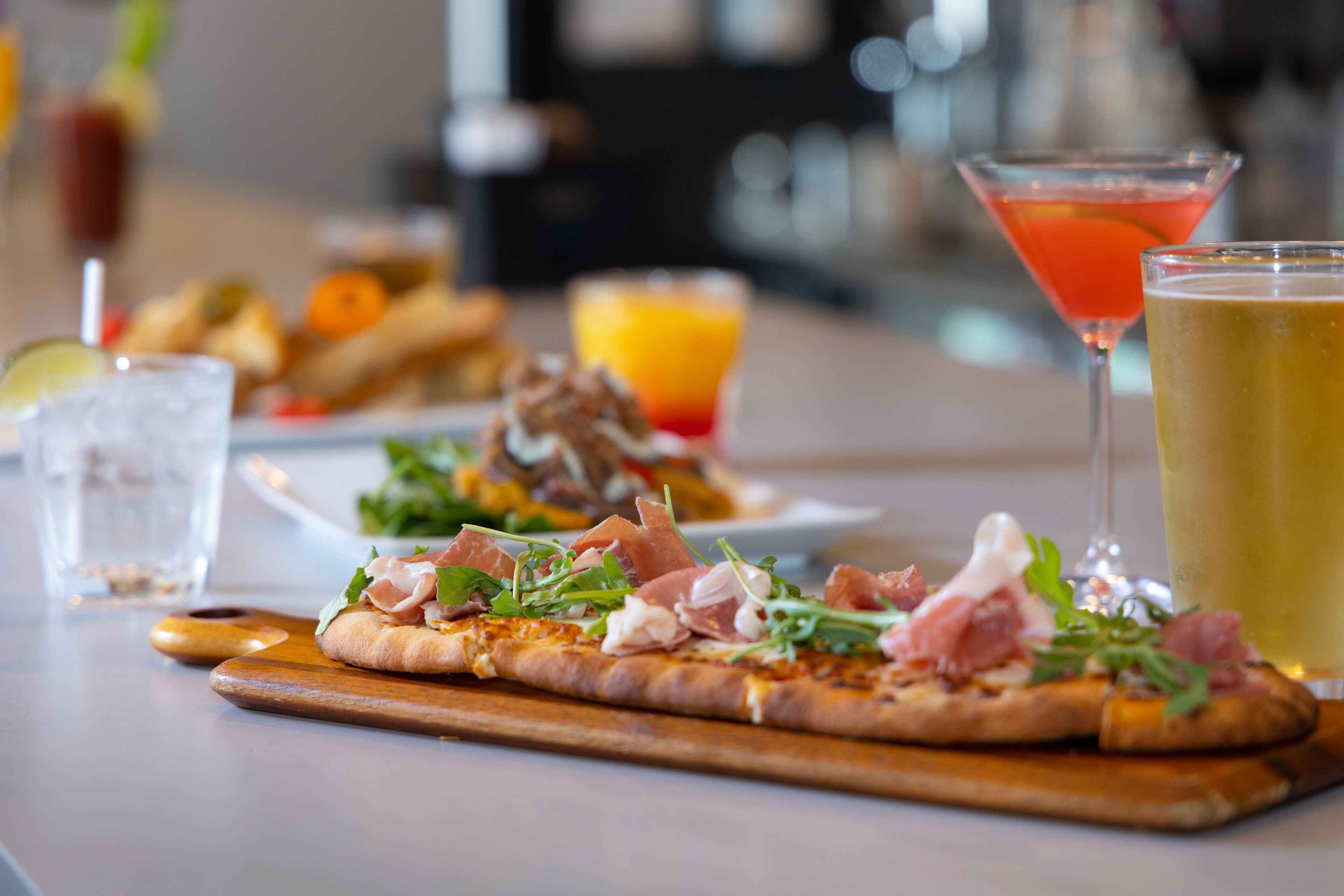 Una pizza con jamón serrano y hojas verdes sobre una tabla de madera.