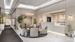 A modern lobby with a reception desk, seating area, and potted plants. - Fortune House Hotel Suites (Miami)