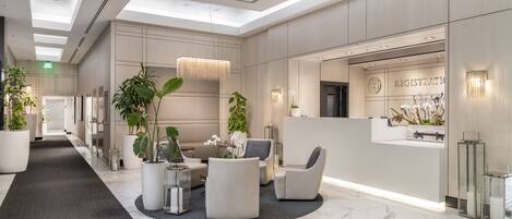 A modern lobby with a reception desk, seating area, and potted plants.