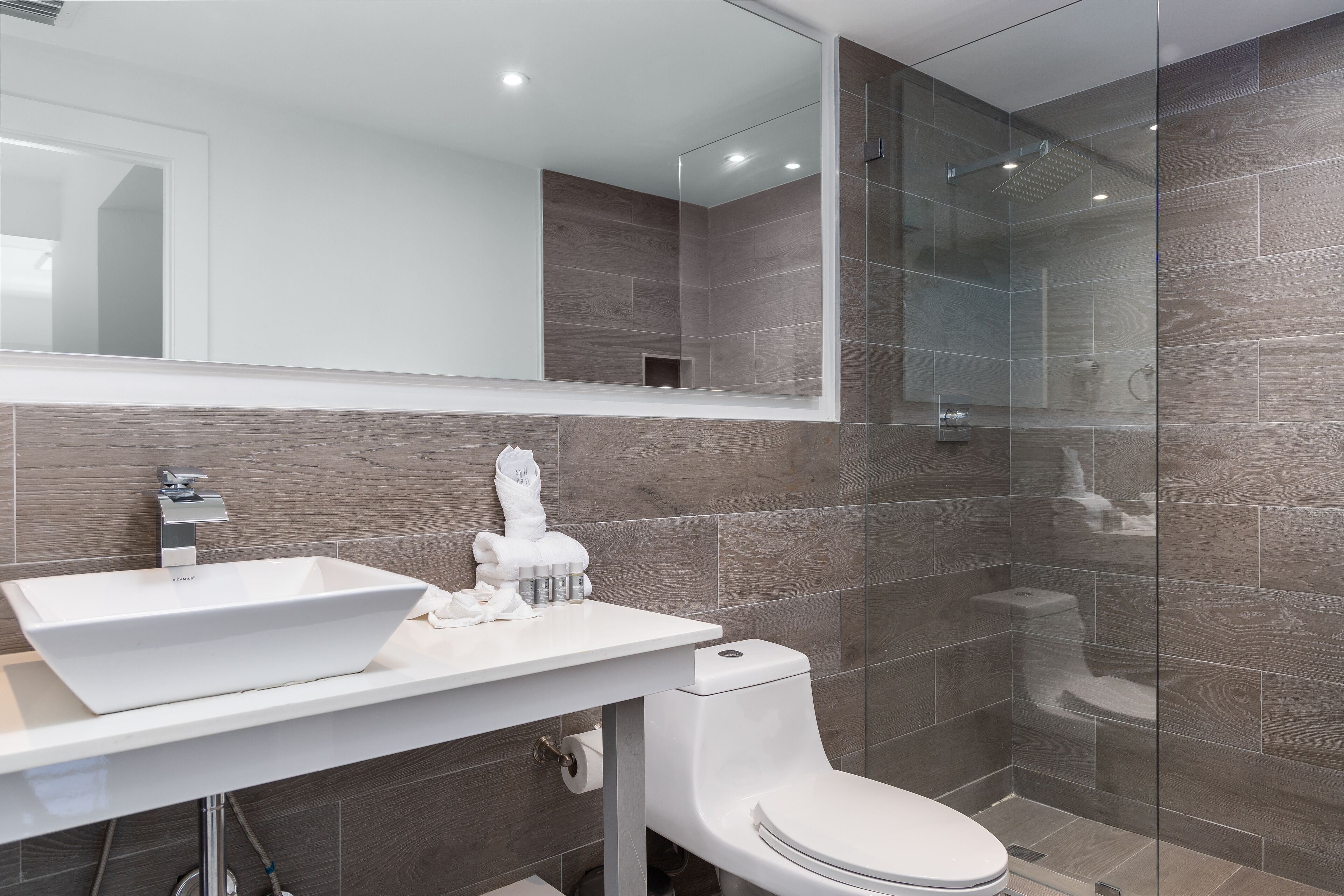 Un baño moderno con un espejo grande, un lavamanos blanco y una ducha con cerramiento de vidrio.
