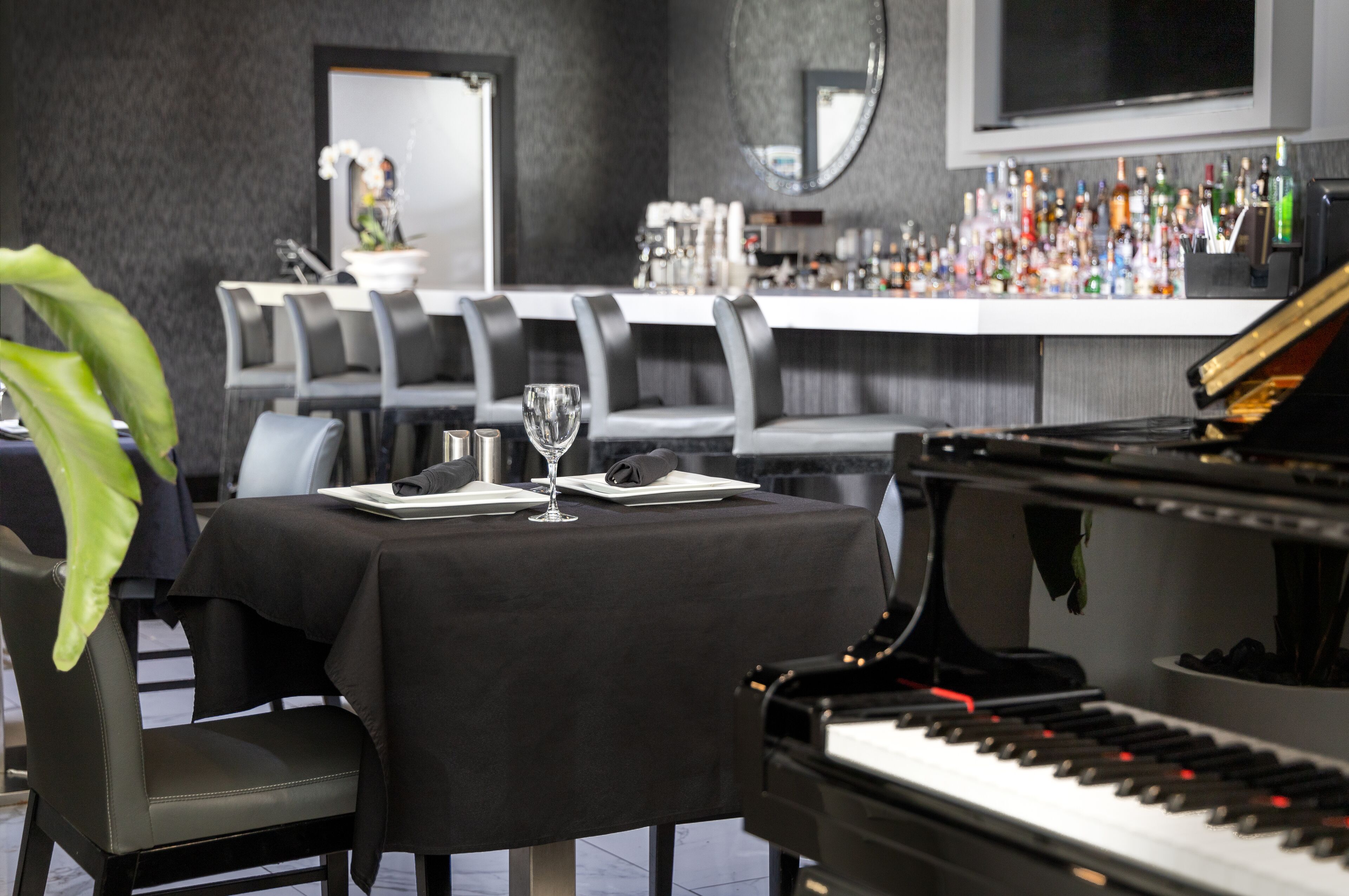 Un área de comedor con un piano, una barra con varias botellas y un espejo grande en la pared.