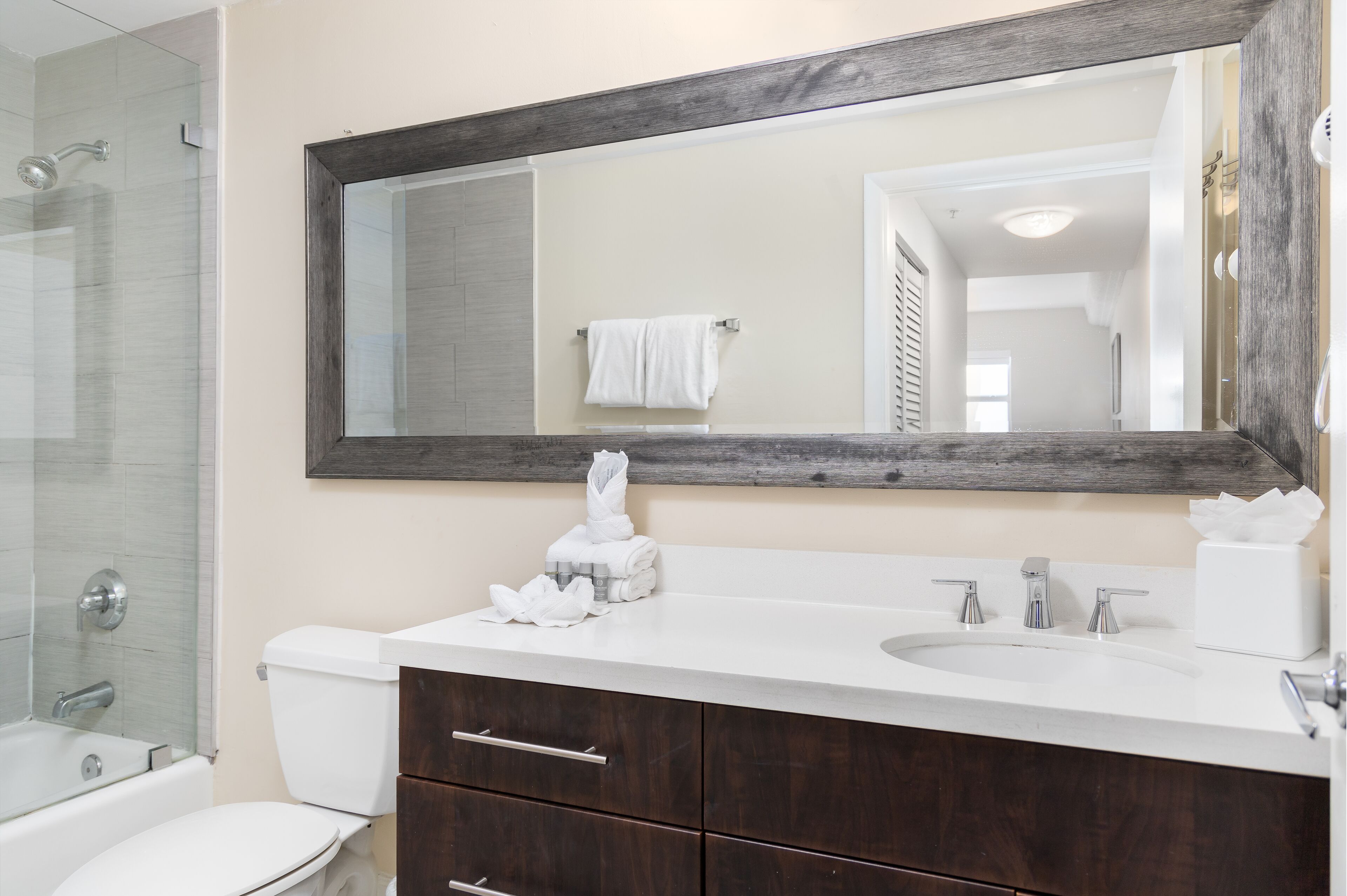 A bathroom with a large mirror, white sink, and dark wooden cabinet.