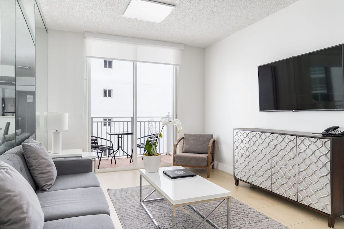 A modern living room with a grey sofa, a white coffee table, a patterned cabinet, and a flat-screen TV mounted on the wall.