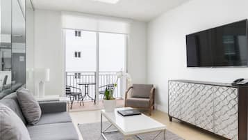 Un salon moderne avec un canapé gris, une table basse blanche, un meuble à motifs et un téléviseur à écran plat fixé au mur.