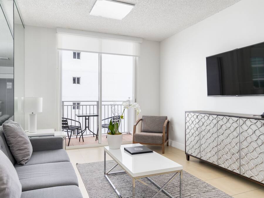 Un salon moderne avec un canapé gris, une table basse blanche, un meuble à motifs et un téléviseur à écran plat fixé au mur.