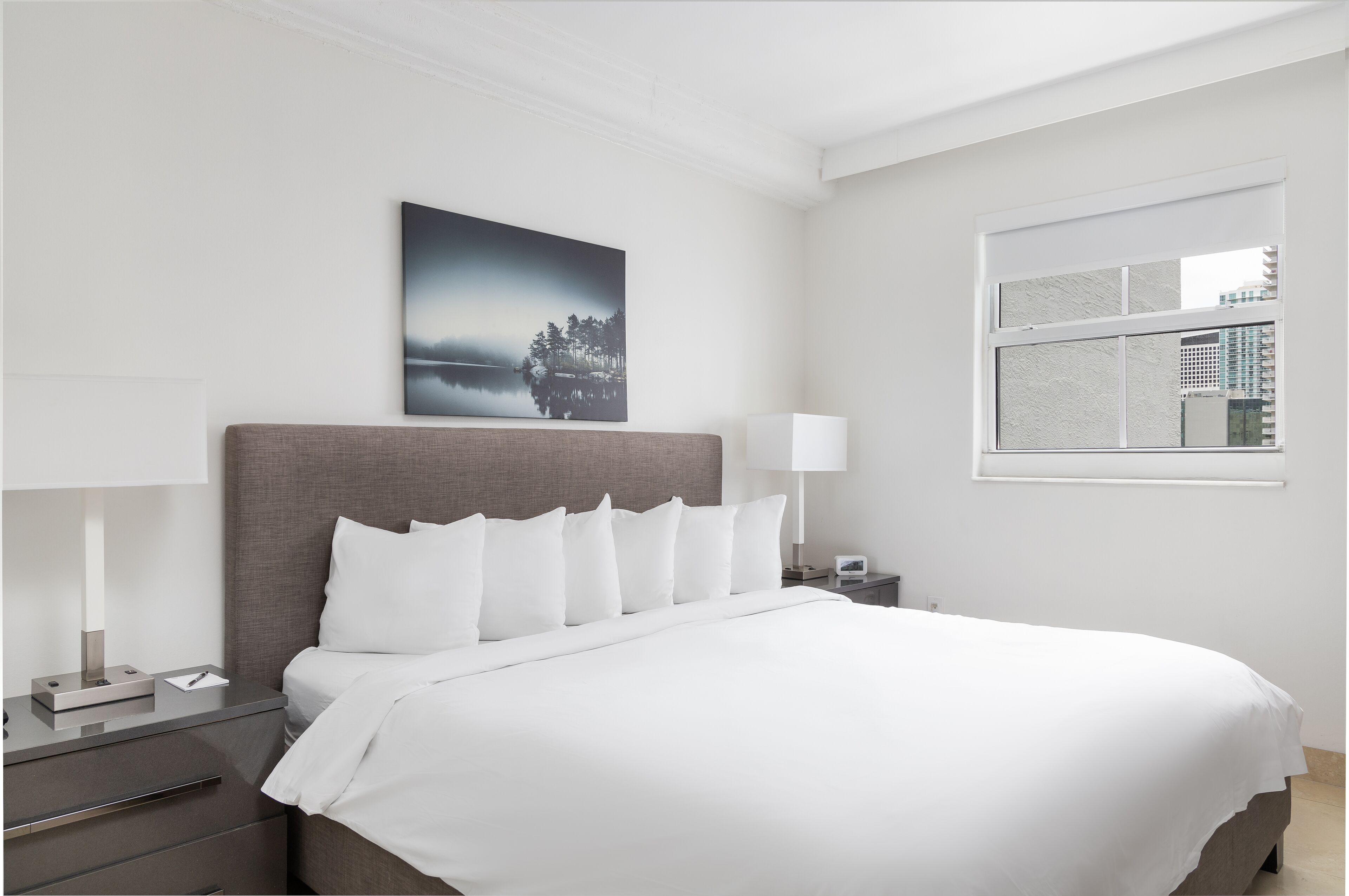 Een moderne hotelkamer met een groot bed, een nachtkastje, een lamp en een raam met uitzicht op de stad.