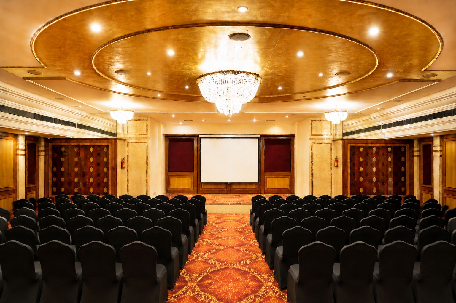 Un salón de conferencias con filas de sillas, una pantalla grande y una araña.