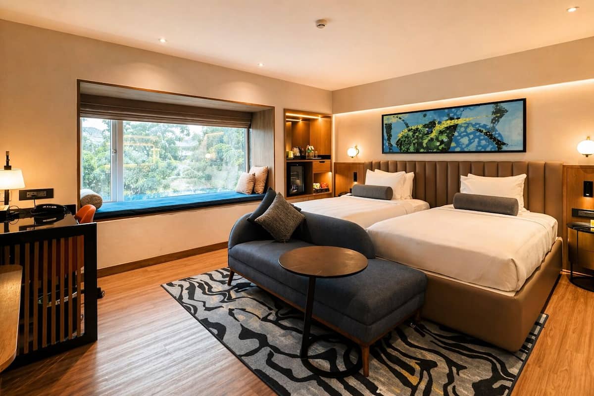 A modern hotel room with a large bed, a sofa, a small table, a desk, a window with a view, and a painting on the wall.