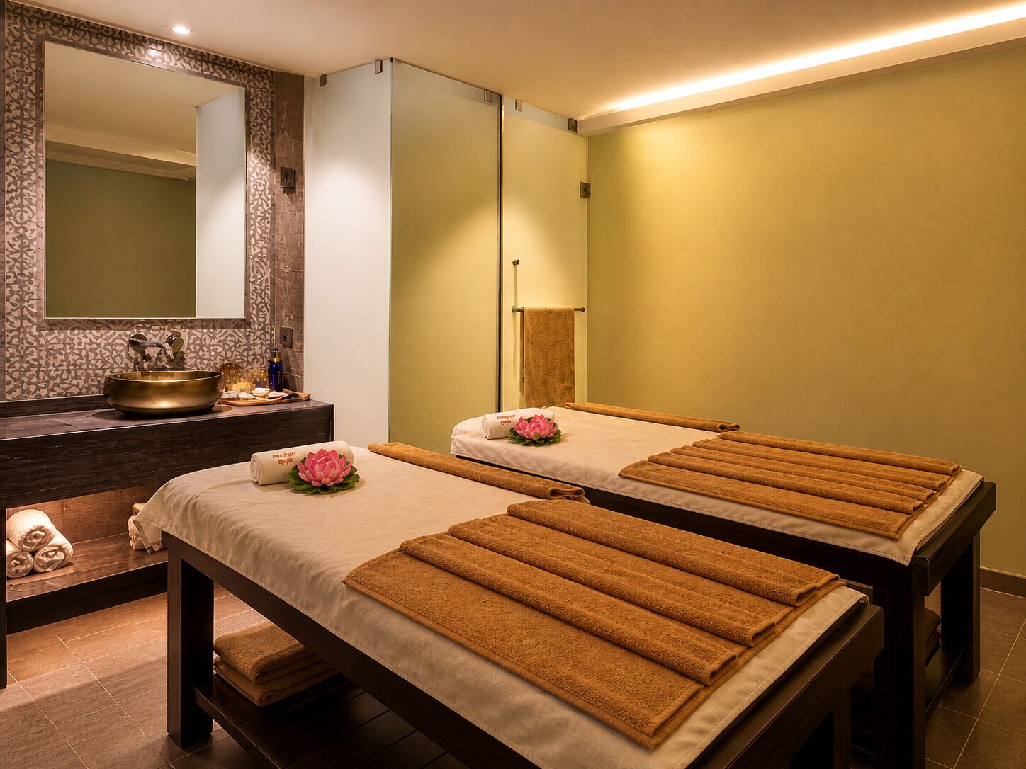 Un cuarto de spa con dos camillas de masaje, un espejo grande y un lavamanos decorativo.