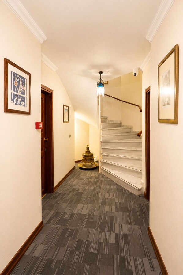 A hallway with a staircase leading to a second floor, framed artwork on the walls, and a patterned carpet. - Sarı Konak Hotel Sultanahmet (Istanbul)