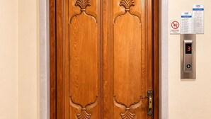 Una porta doppia in legno con pannelli decorativi e un pannello di controllo dell'ascensore digitale con il numero '3' visualizzato.