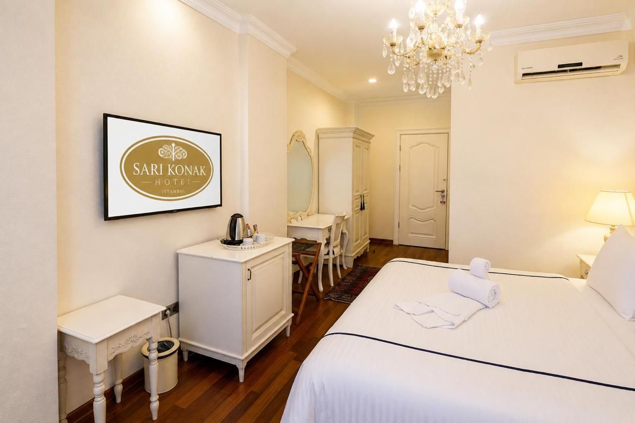 Een hotelkamer met een bed, een bureau, een stoel, een kledingkast, een spiegel en een kroonluchter.