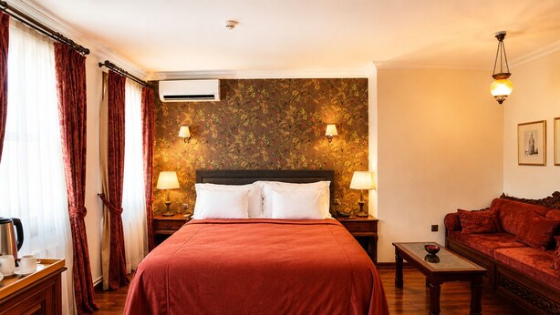 Una camera d'albergo con un letto grande, due lampade ai comodini, un divano, un tavolino e un condizionatore d'aria a parete.
