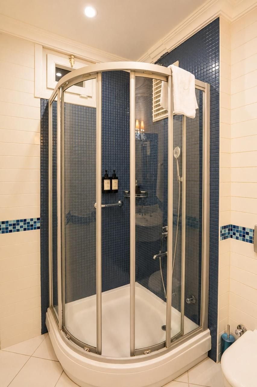 A corner shower with a glass enclosure, a white bathtub, and blue-tiled walls.