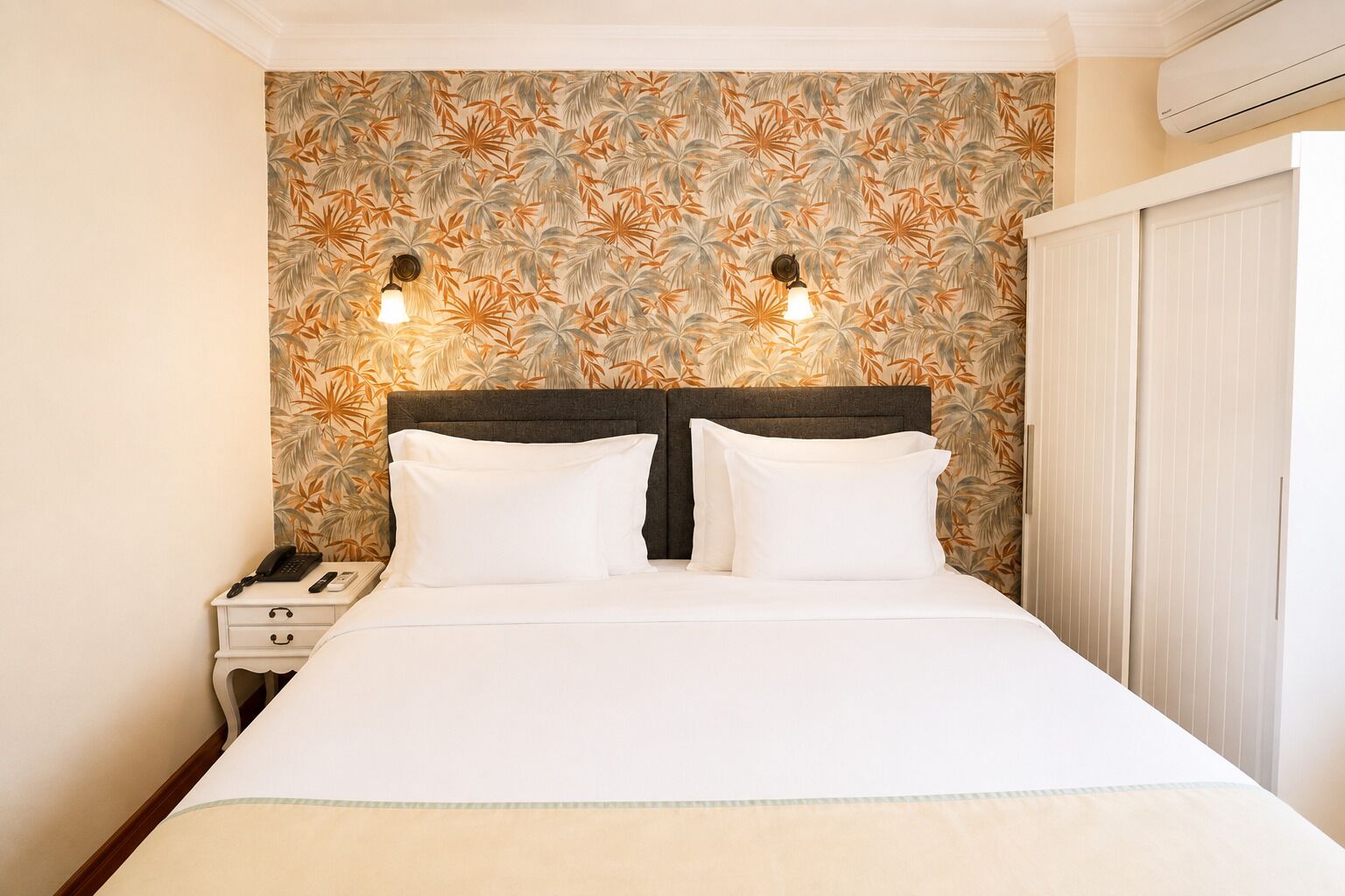 A hotel room with a bed, two bedside lamps, a nightstand, and a wardrobe.