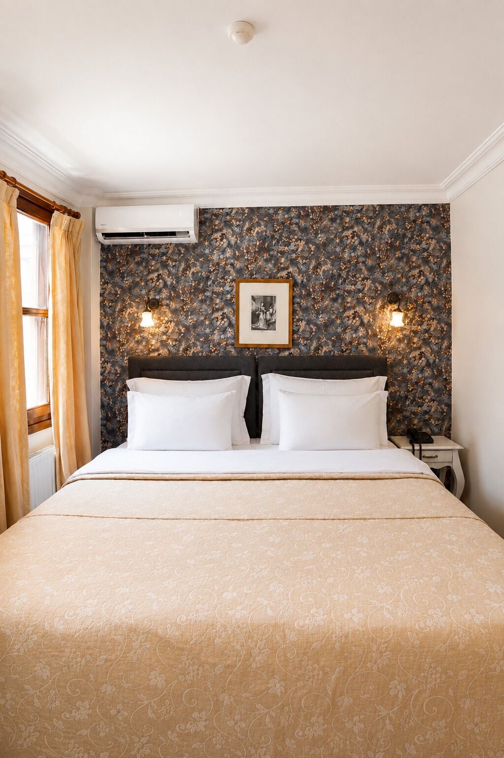 A hotel room with a large bed, two bedside lamps, a framed picture on the wall, and an air conditioning unit.