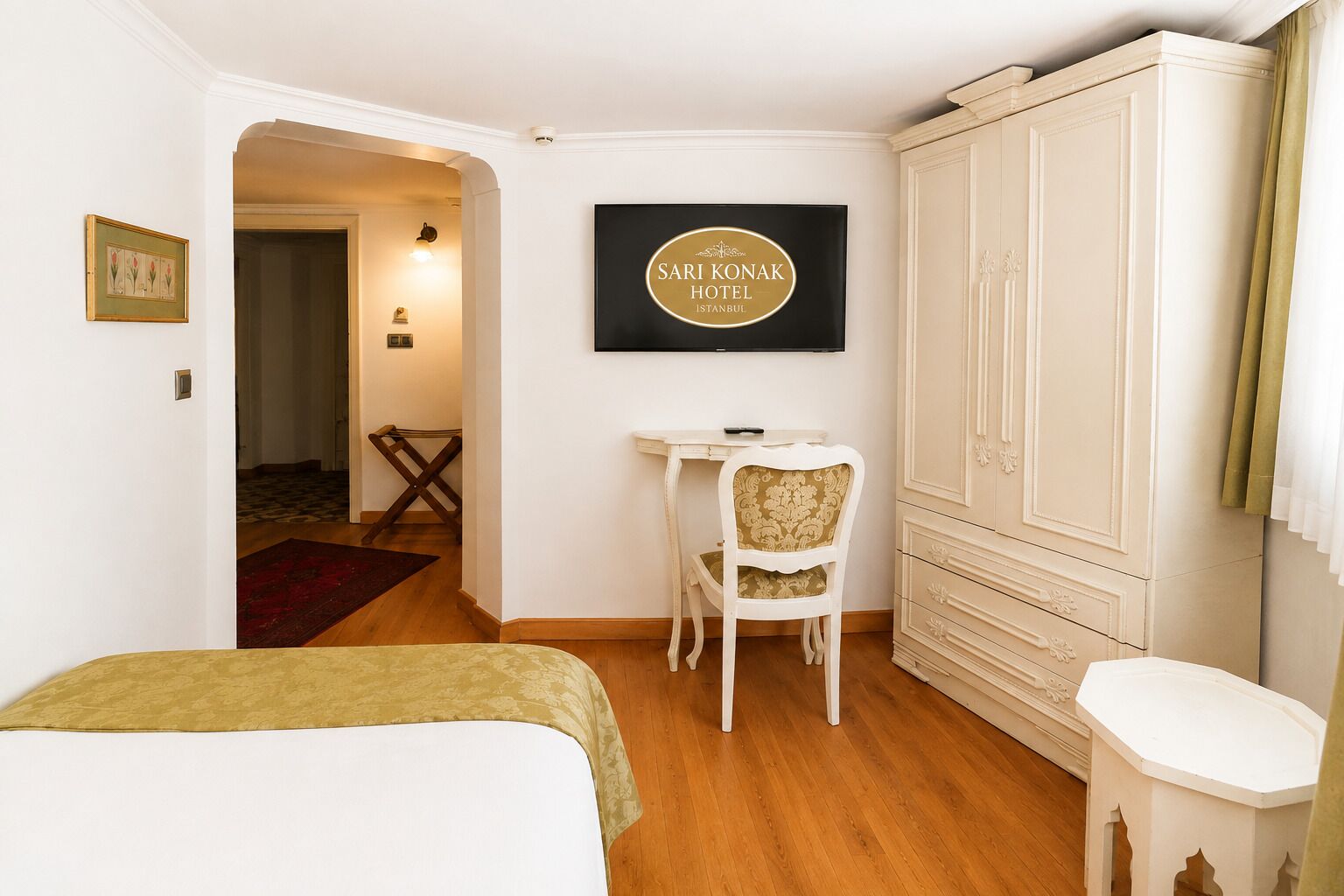 Una habitación de hotel con una cama, un escritorio, una silla y un armario. Hay un letrero en la pared con el nombre del hotel.