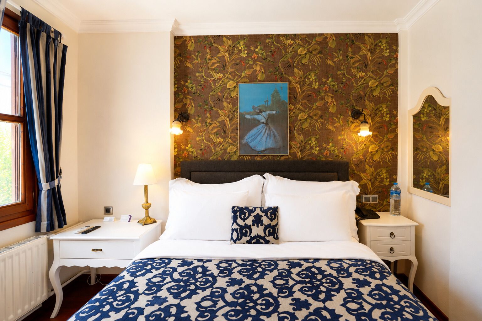 A hotel room with a bed, nightstands, a lamp, a painting, and a mirror.