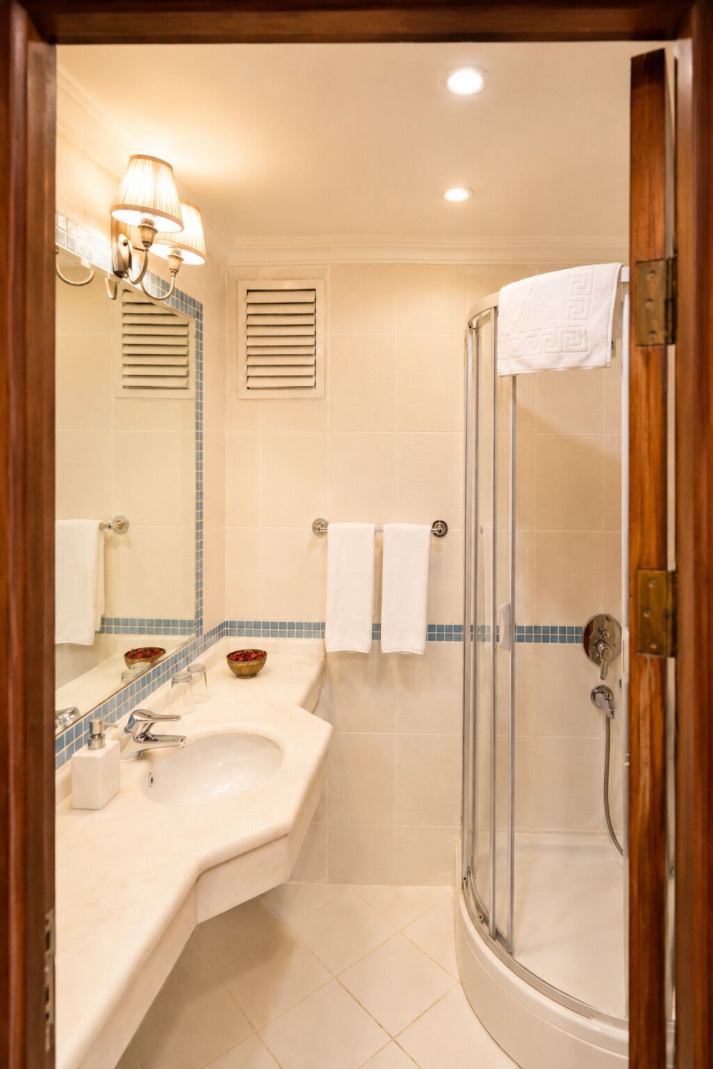 Un baño con lavamanos, espejo, toallero, ducha y lámpara.