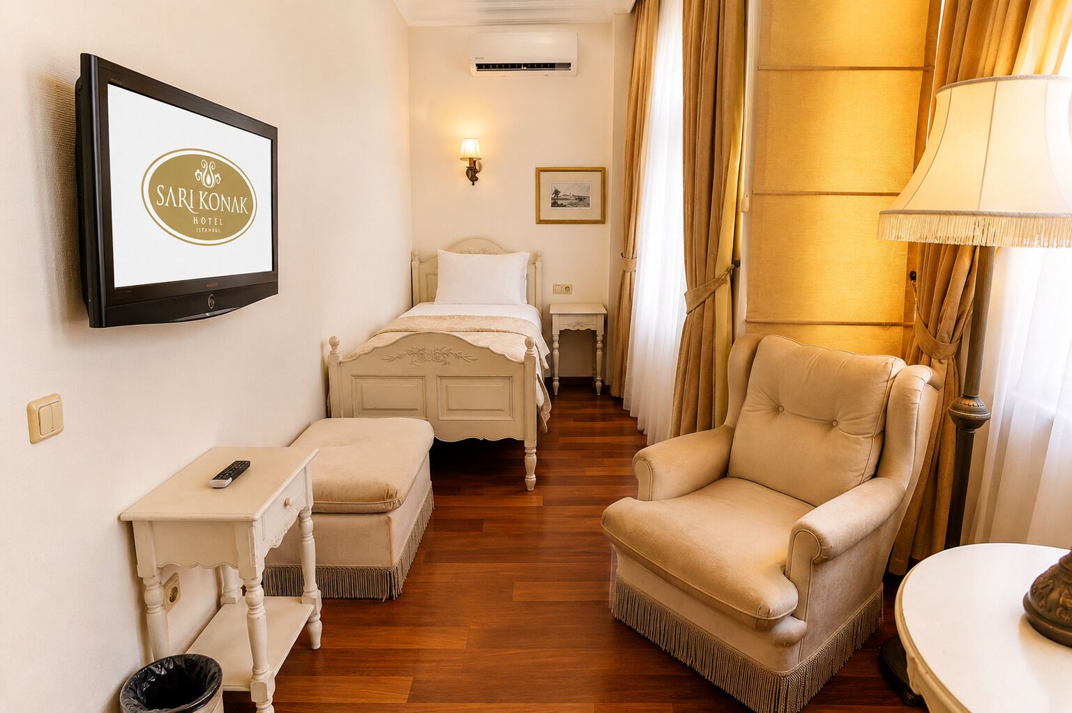 A hotel room with a bed, a chair, a small table, a TV, and a lamp.